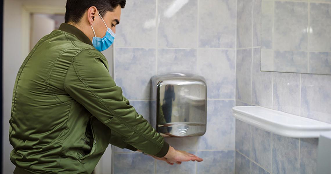 Man wearing a mask washing hands in public restroom
