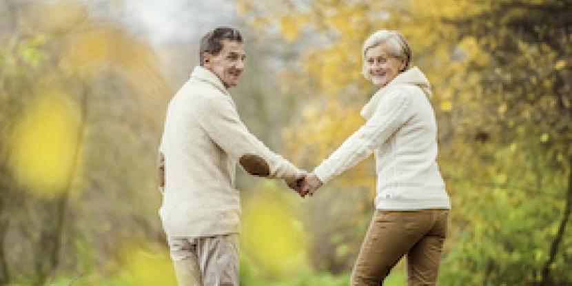 Two seniors holding hands walking on a trail in the fall.