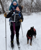 Photo Kaitlin Kessler on skis, with baby and dog