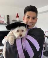 Eric Wu, DMD, dressed in graduation gown, holding his dog wearing his cap