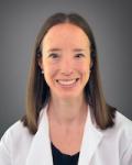 Portrait of Dr. Horn, she is smiling at the camera sitting in front of grey background. She is wearing a black shirt under her white coat.