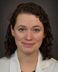 Headshot of a female provider. Alyssa Robinson, APRN has shoulder-length brown hair and is wearing a black blouse under white coat. She is sitting in front of a light grey background.