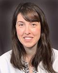 headshot of Kristen Lanpher, a neurosurgical physician assistant at UVM Medical Center. She is wearing a white coat, has long brown hair, and sitting against a dark grey background.