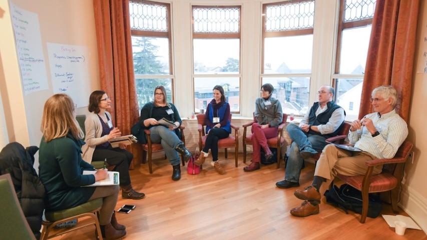 Workshop attendees in discussion sit in a half circle. 