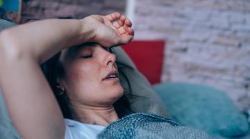 Woman sick in bed with the flu with her arm on her forehead.